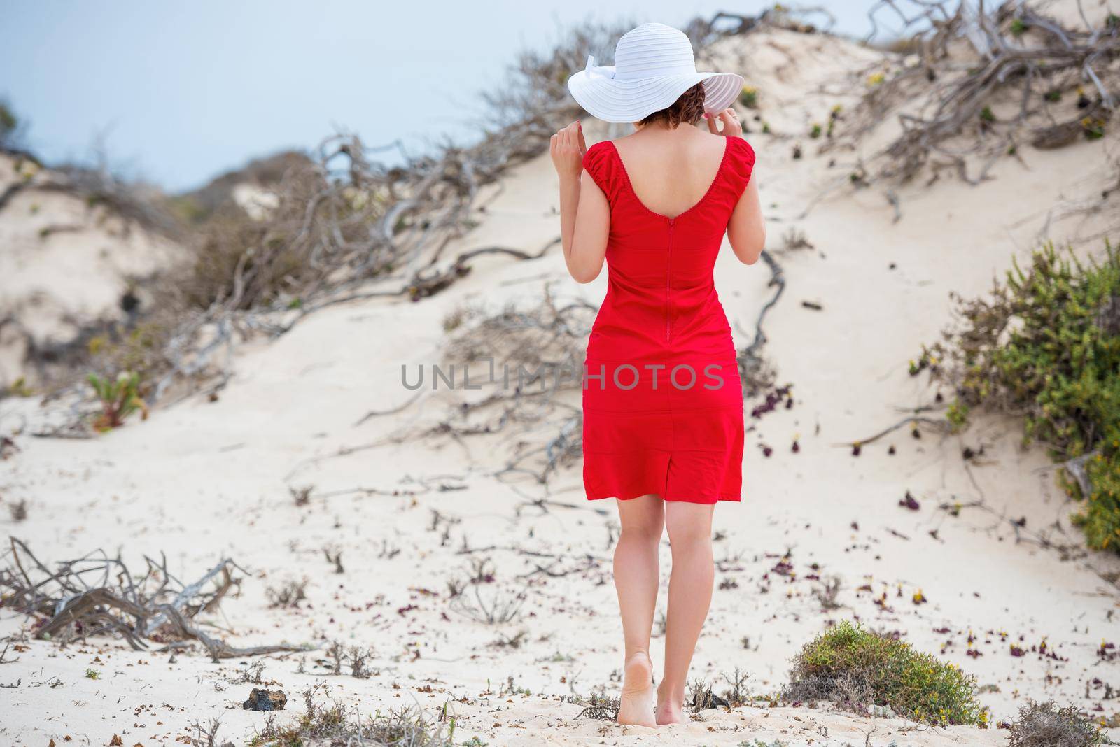 beautiful young woman in evening red dress and white hat on a background of a sand desert