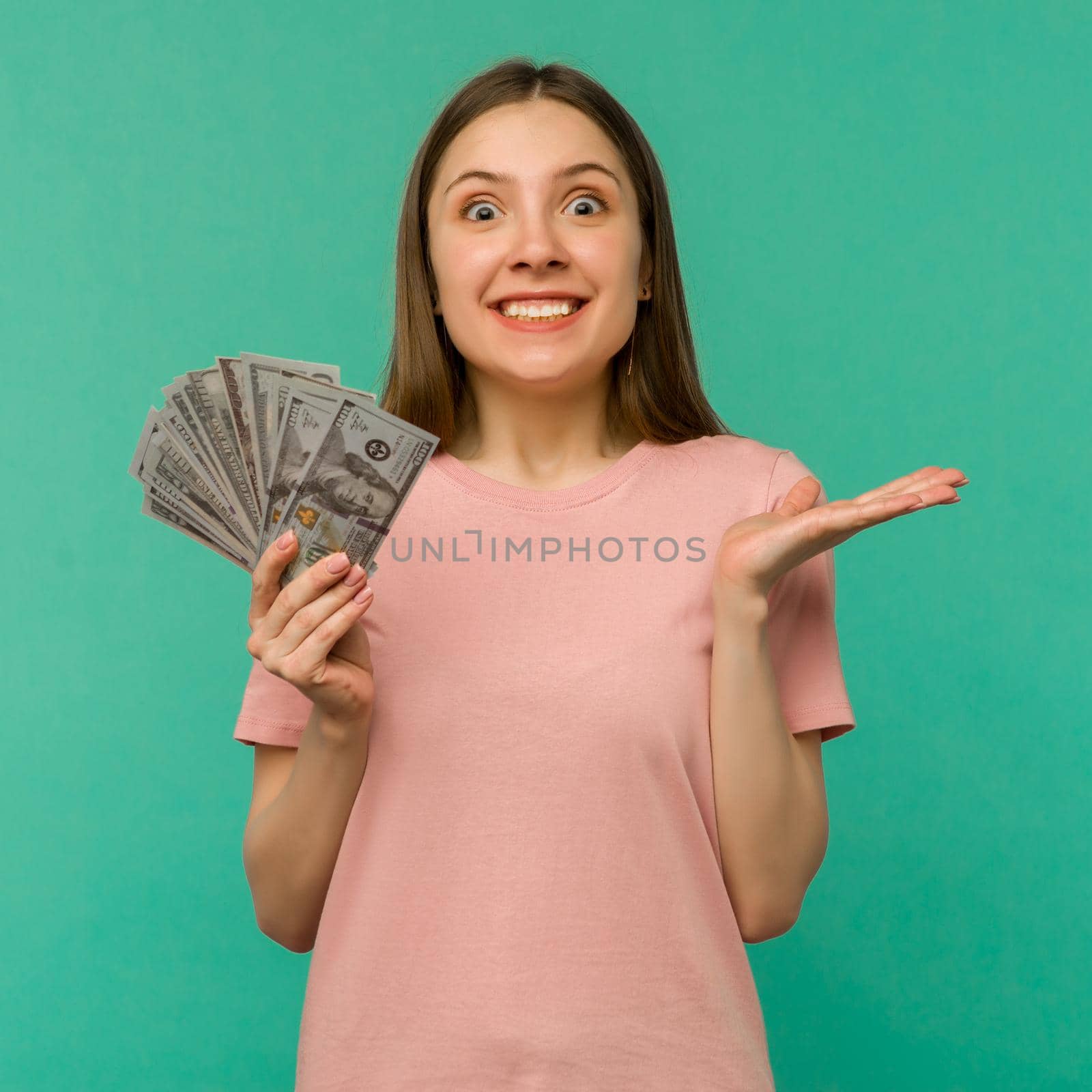 Portrait of a cheerful young woman holding money banknotes and celebrating isolated on blue background