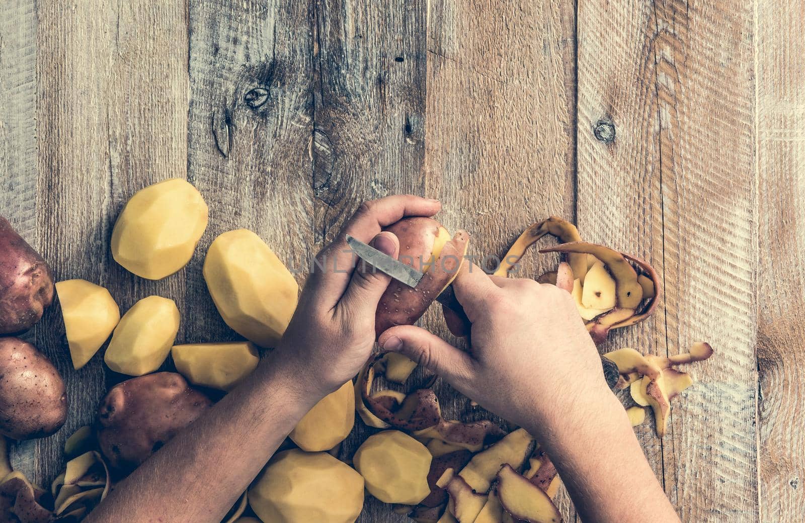 hands peeling potato on wooden board
