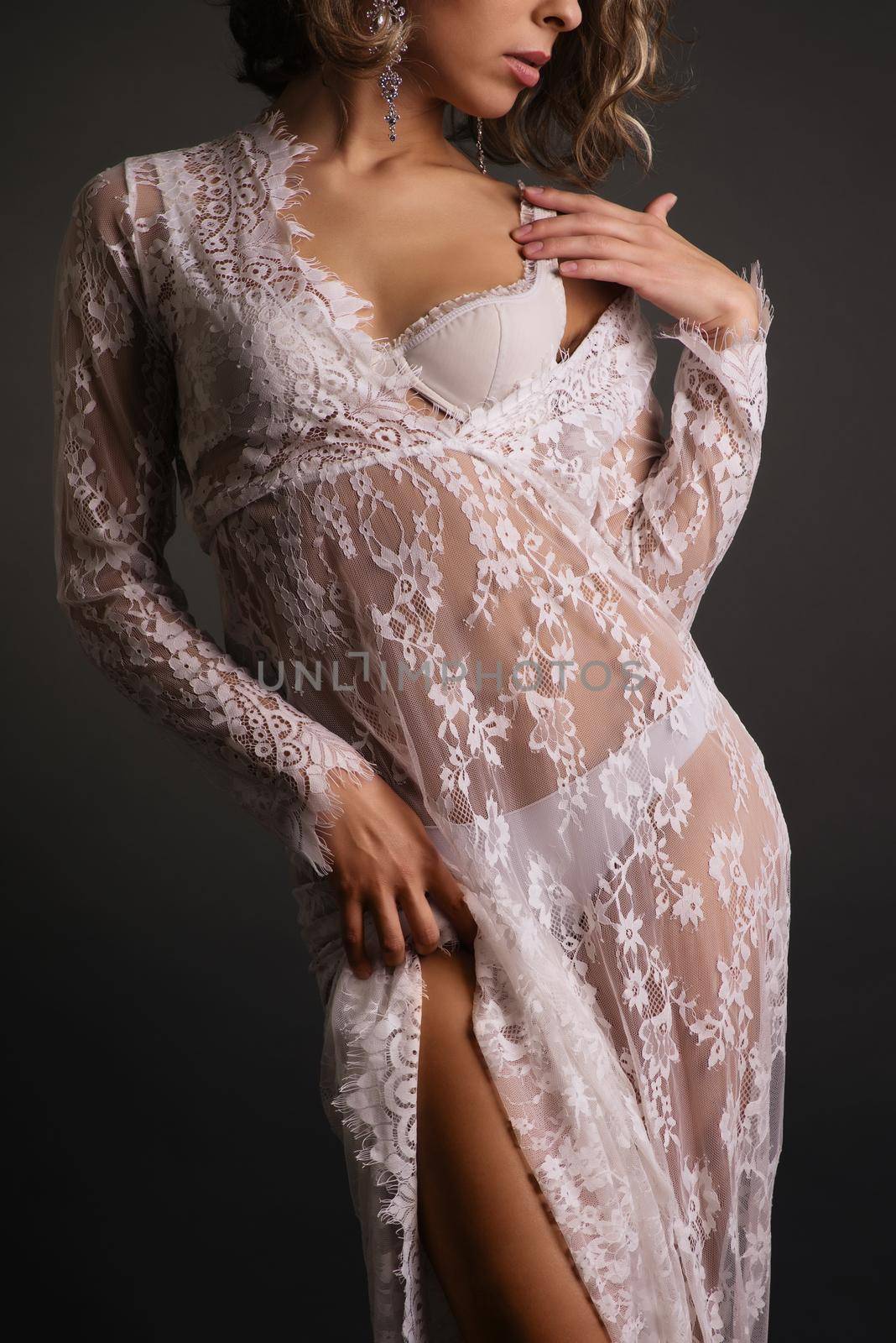 Close up body of young slim woman in white lace transparent dress on dark background