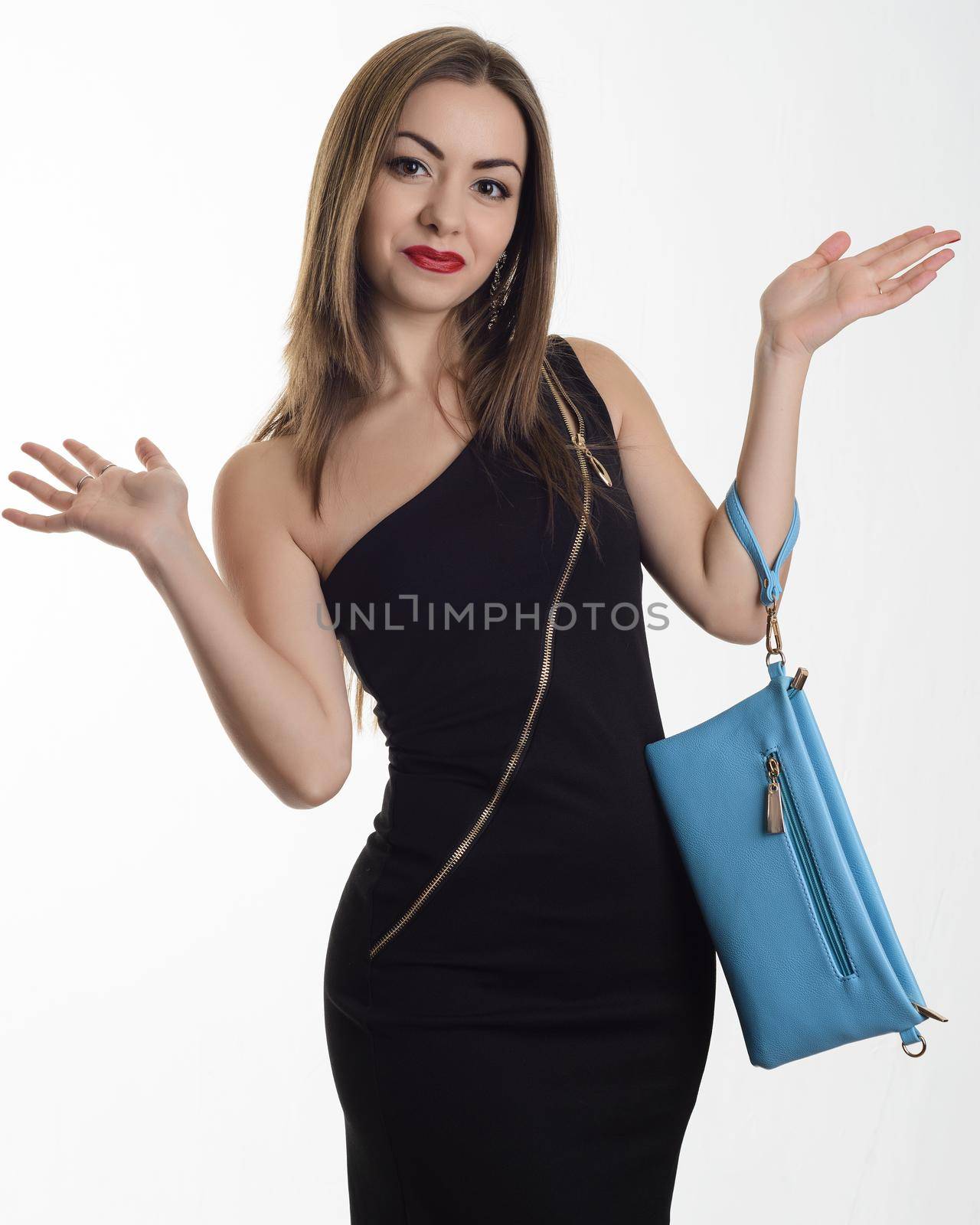 Stylish young woman in a black evening dress with a blue clutch standing hands outstretched to the sides of surprise by zartarn