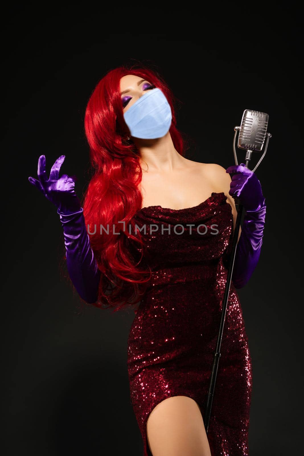 Young romantic redhead woman in mask with very long hair in red dress with microphone on the stand sings with his eyes closed on a black background. by zartarn