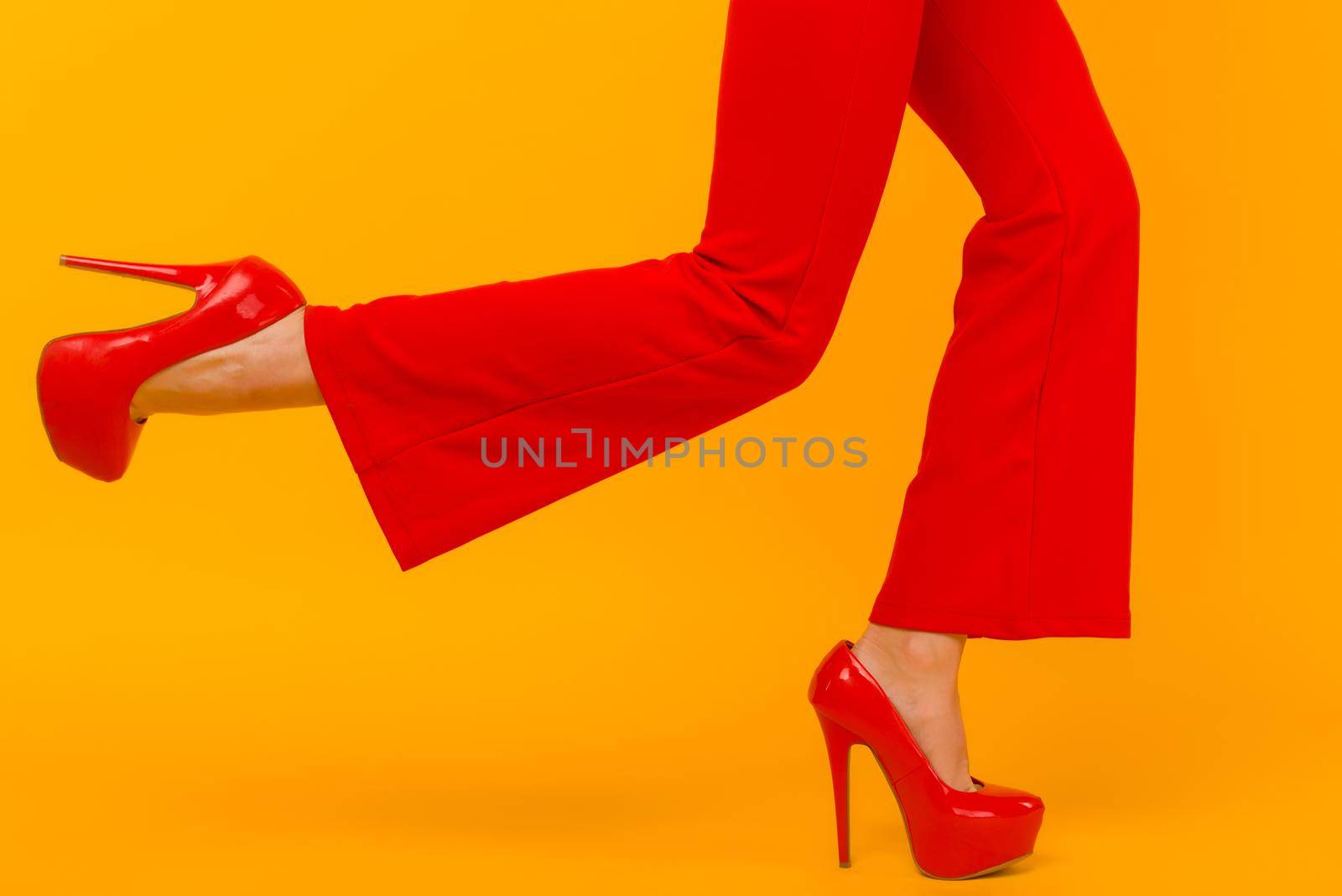 The business woman running somewhere hurrying up isolated on yelow background. Stylish red heels and pants on thin female legs