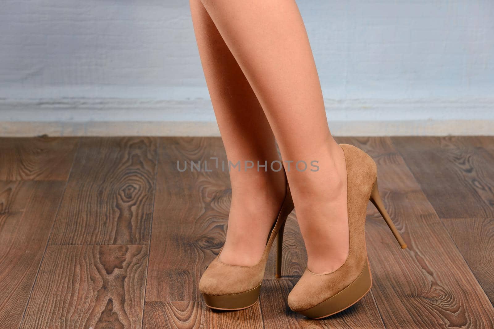 Girl in beige suede high-heeled shoes on the wooden floor