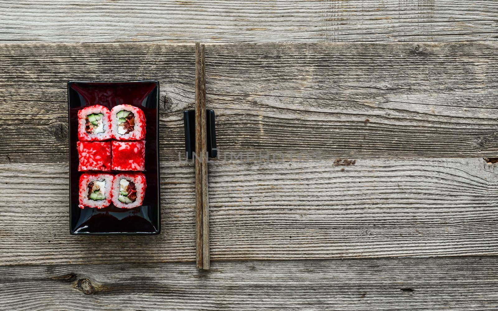 sushi on square black plate with chopsticks on wooden background
