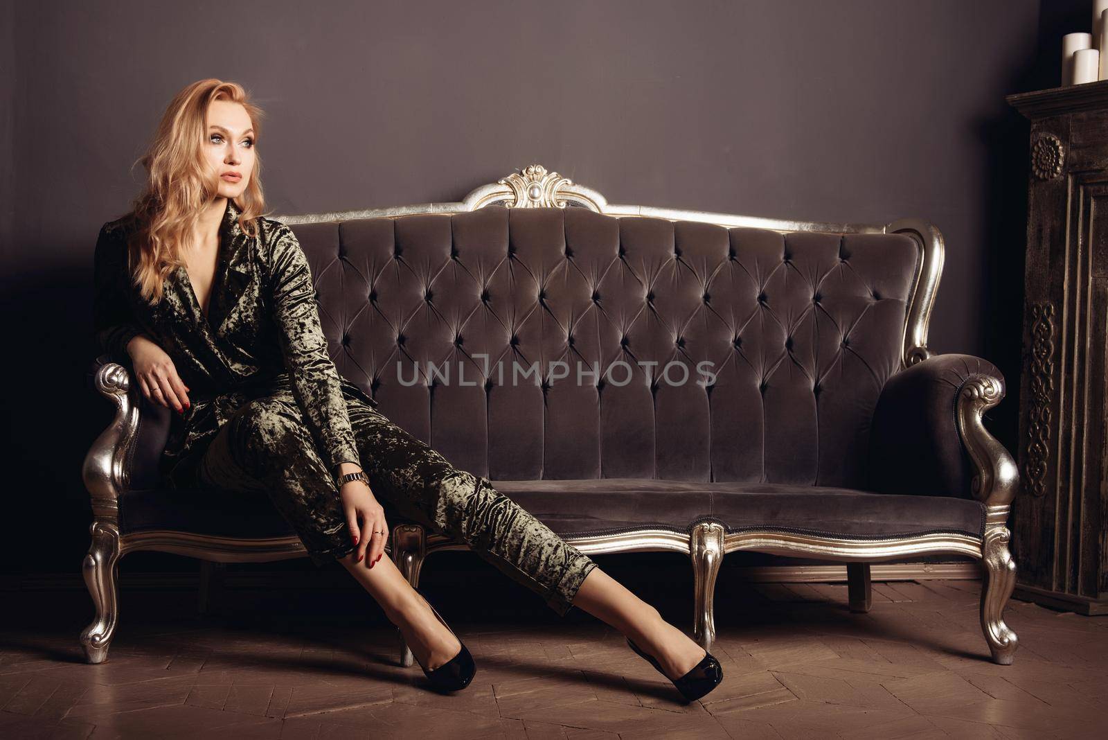Beautiful young woman in a velor suit sits on a vintage sofa.