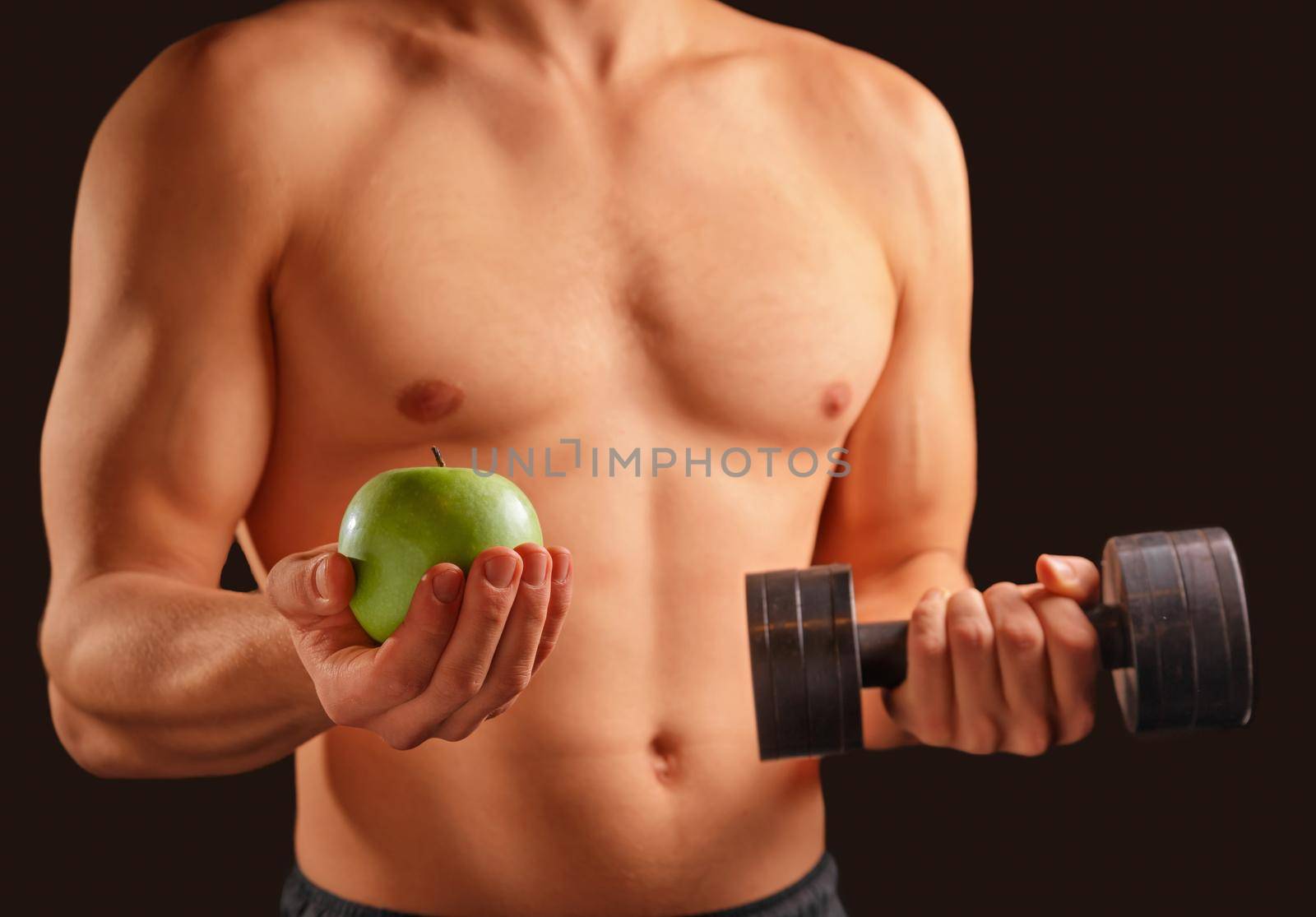 Unrecognizable man holds green apple and dumbbell, concept of healthy life