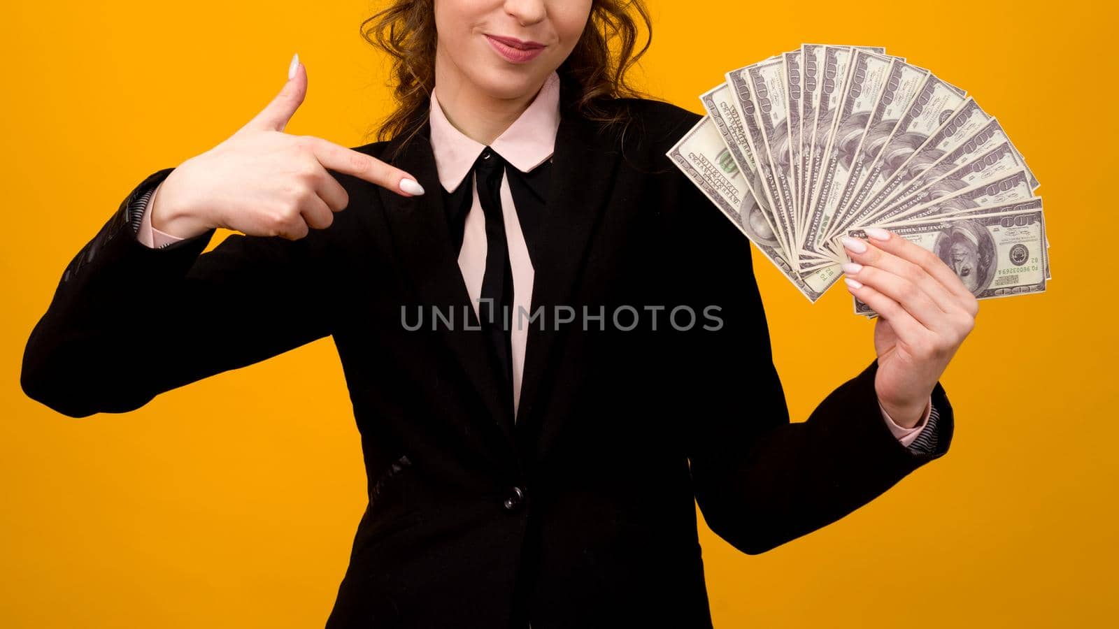 Woman pointing towards a stack of money with her finger isolated on yellow background.