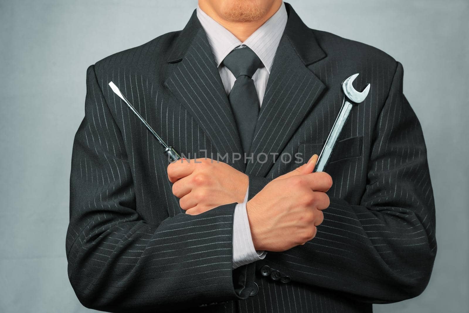 Businessman in a suit holds metal wrench and screwdriver, concept of business creation