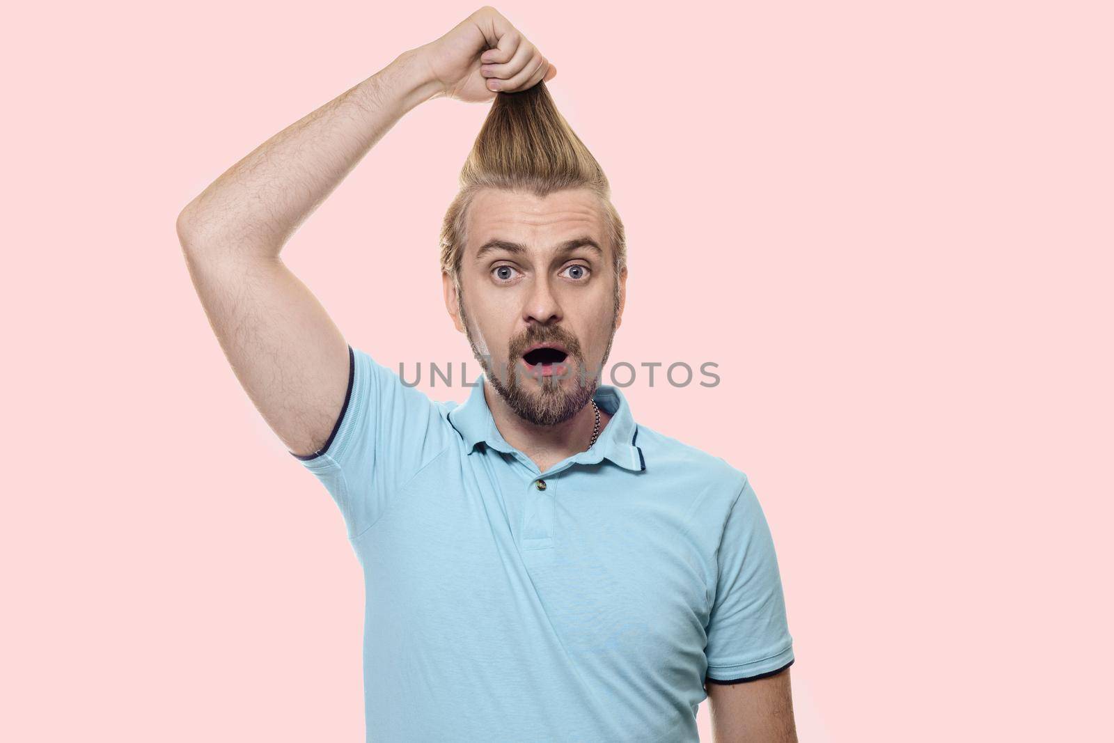 Attractive man in a turquoise T-shirt stands with his mouth open in amazement, and pulling his hair to the top