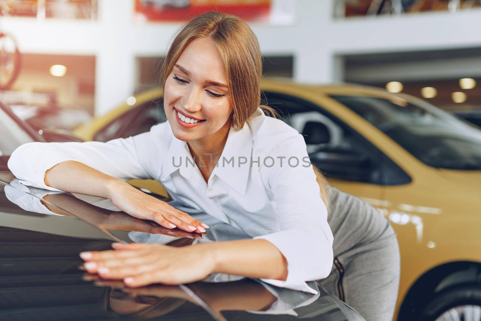 Beautiful young woman touching her new car with pleasure and joy