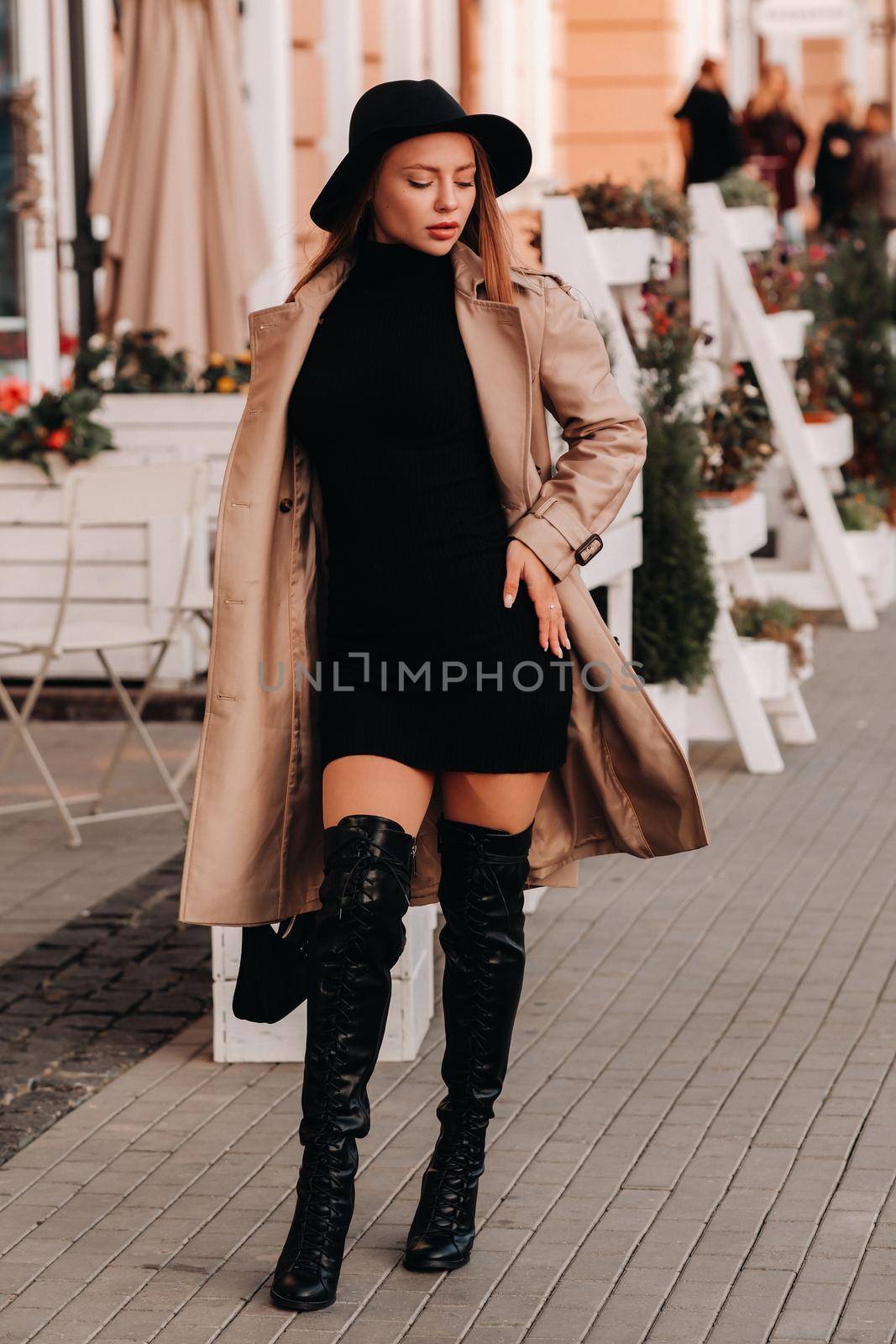 Stylish young woman in a beige coat and black hat and with a black purse on a city street. Women's street fashion. Autumn clothing.Urban style.