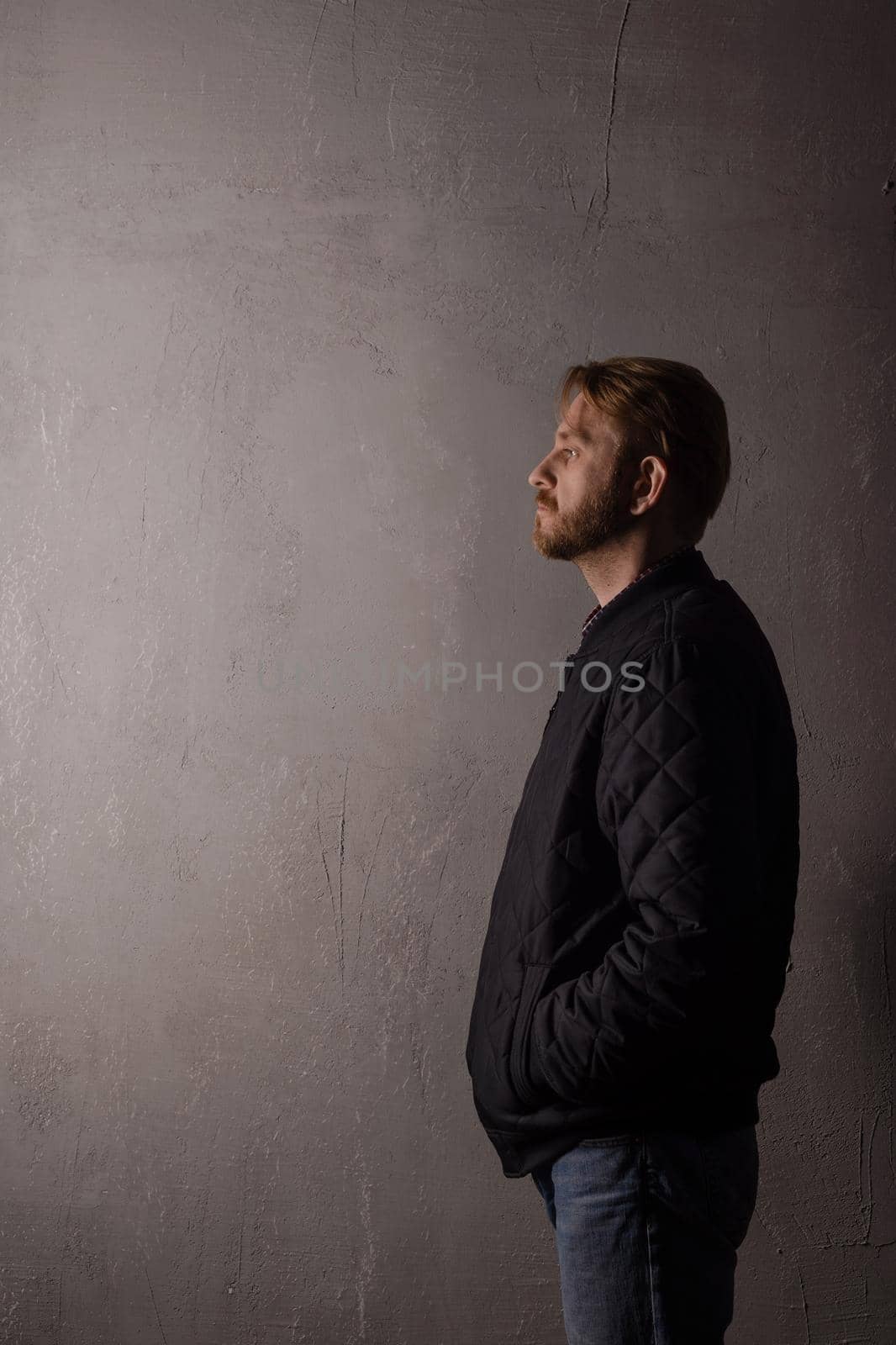 An emotionless portrait of a man in a black jacket and jeans standing near a wall. copy space. deadpan without retouching