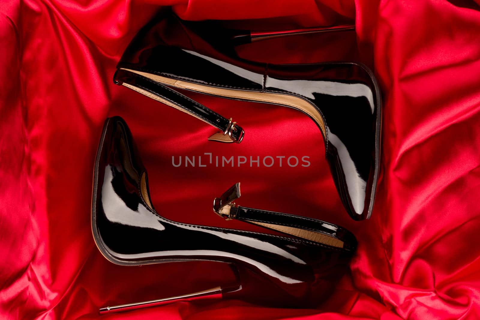 Black fetish shiny patent leather stiletto high heels with ankle strap on red satin background