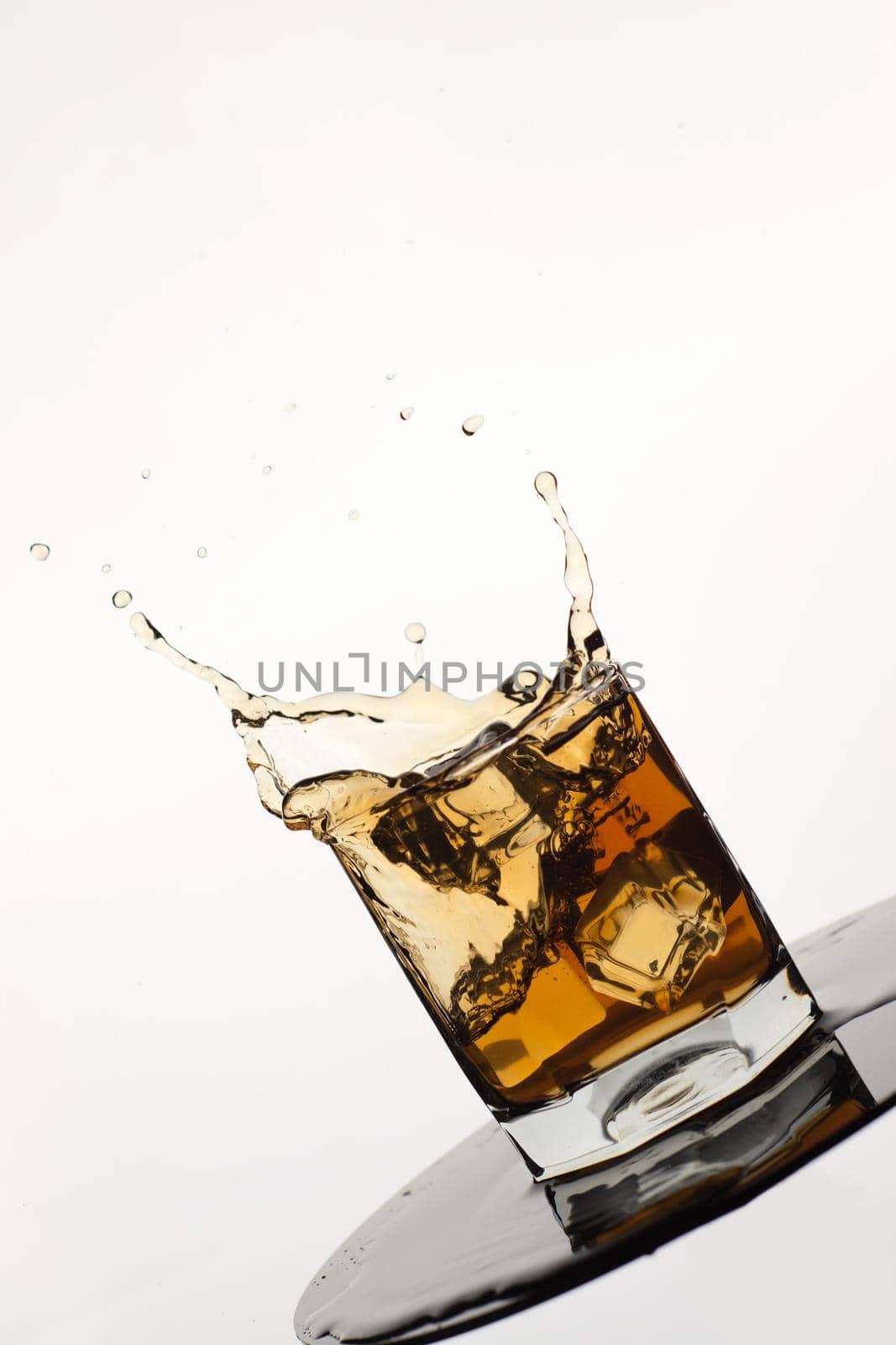 Tilted Glass of splashing whiskey with ice isolated on white by zartarn