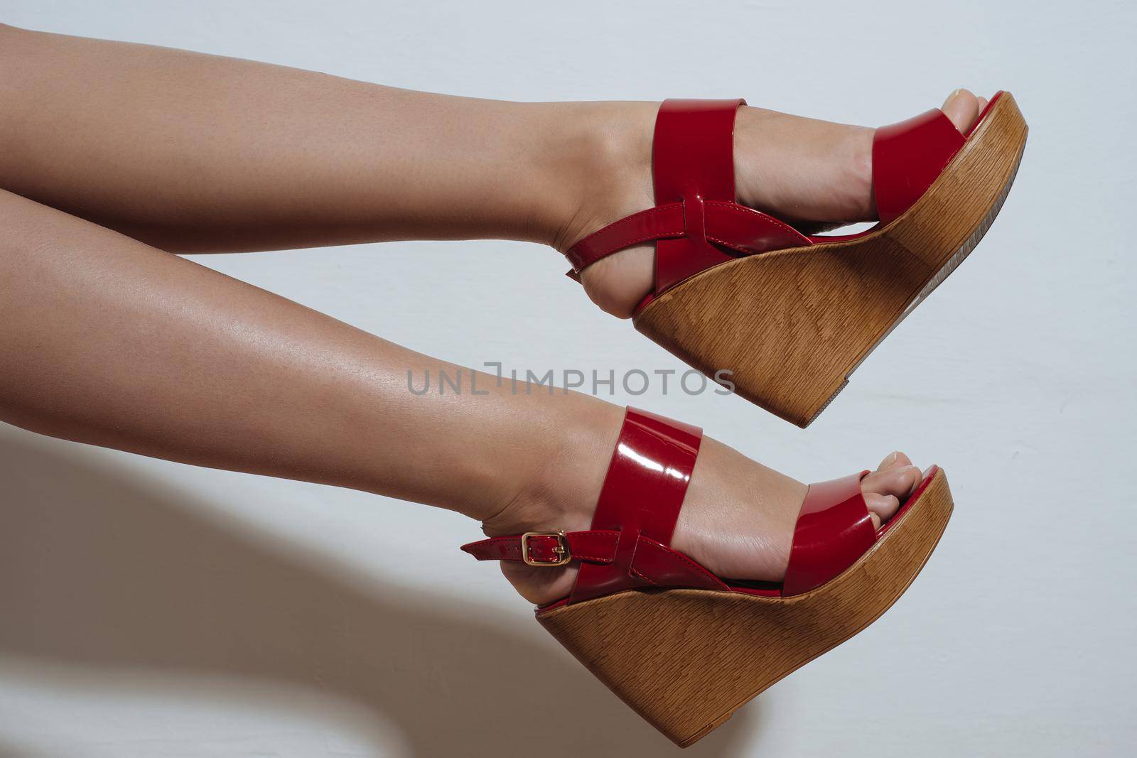 Beautiful female legs in red sandals on a wedge on white background