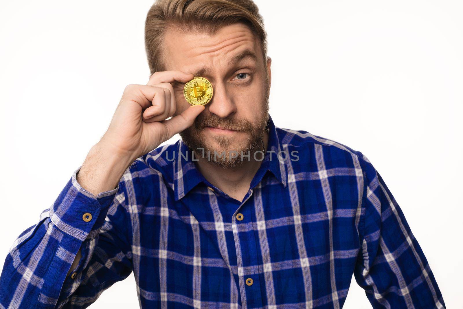 Portrait of a winking man holds a coin bitcoin in front of his eye isolated on white