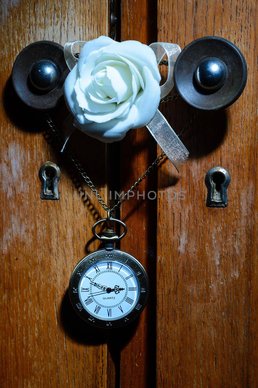 Pocket watch hanging on a chain on a cabinet handle with white rose flower
