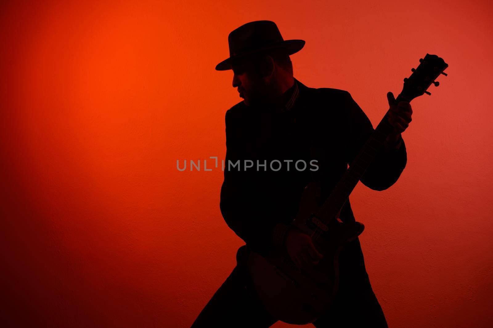 silhouette of a guitarist in a hat on a red background.