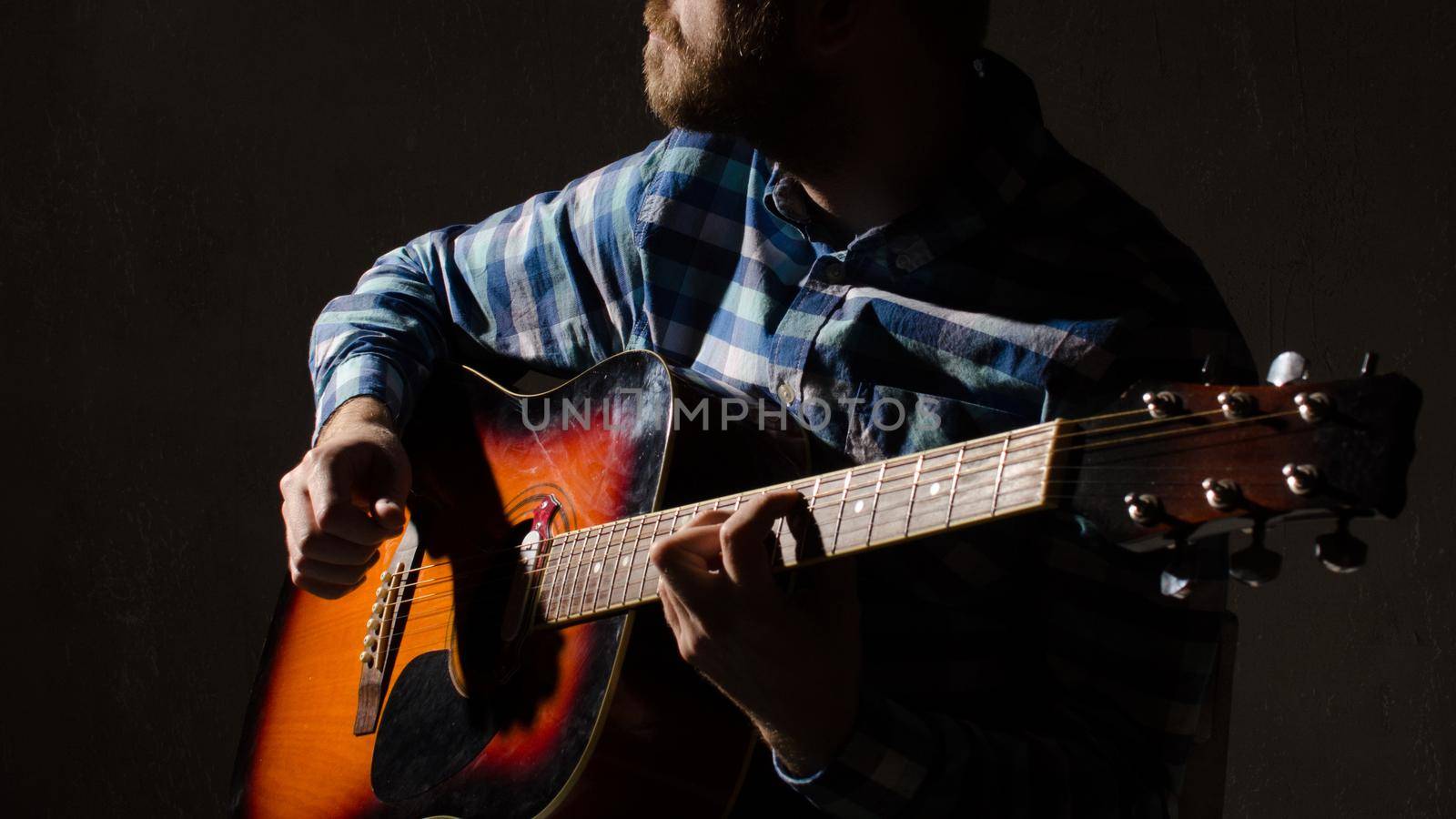 A bearded man in a plaid shirt plays an acoustic guitar. hands close-up.