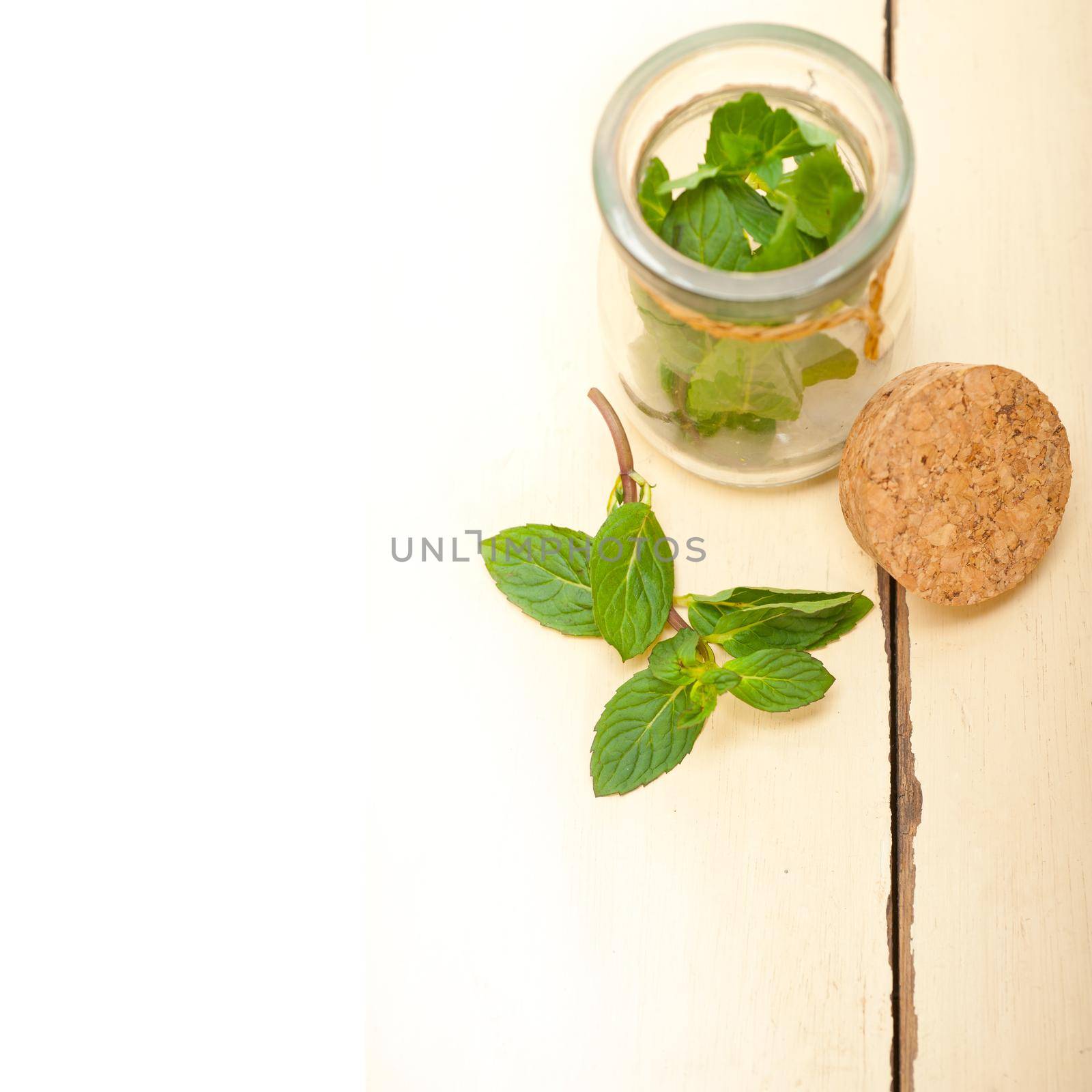 fresh mint leaves on a glass jarover a rustic white wood table