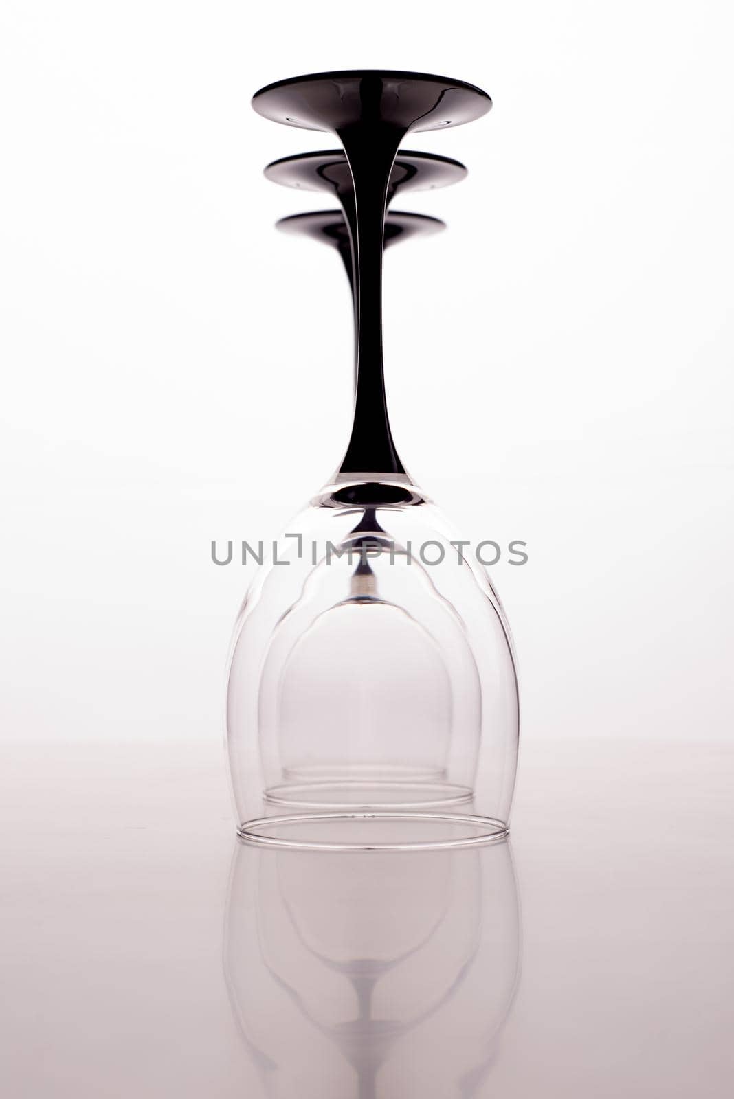 Closeup of three transparent clear crystal empty three inverted wine glasses grey background, vertical picture