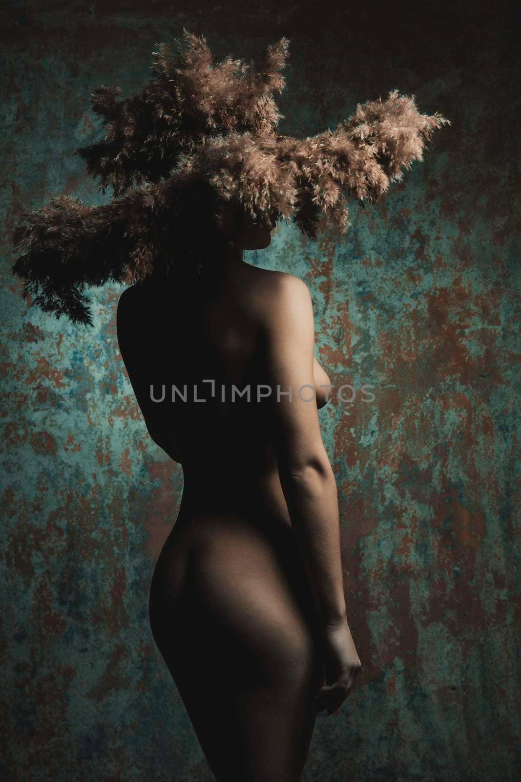 naked girl in a hat of spikelets standing in studio at color wall