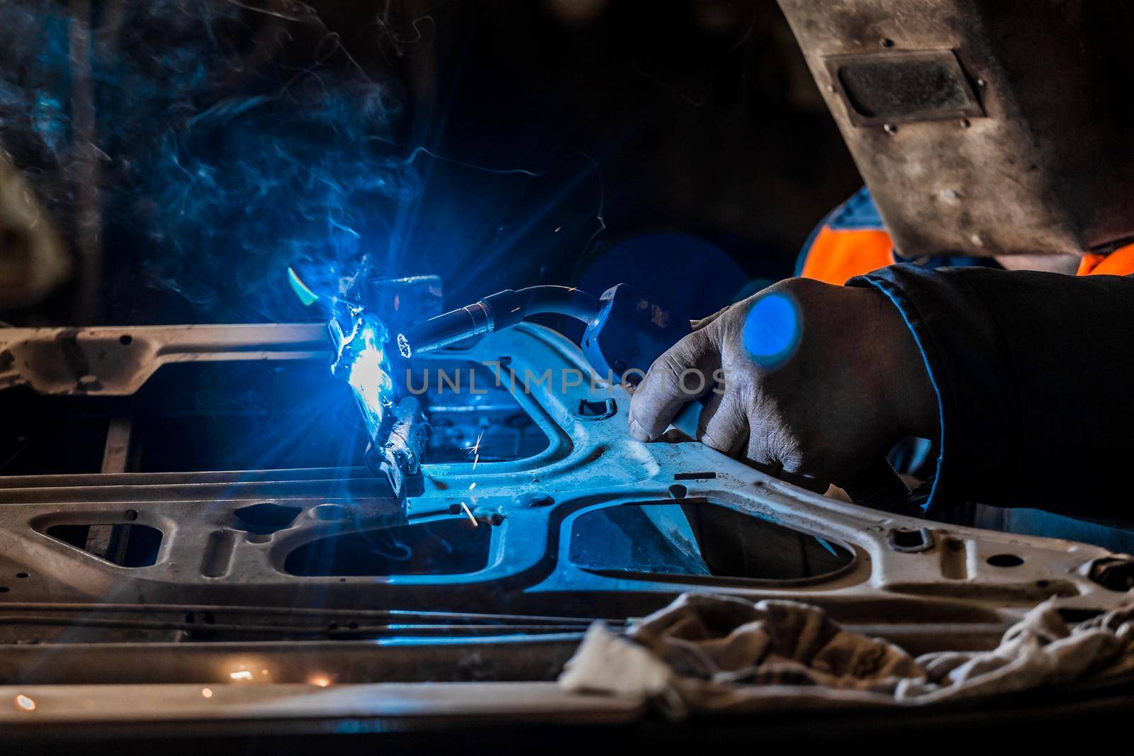 The welder in the protective shield is engaged in welding and metal, work and repair of the automobile door in the workshop of the industrial plant.