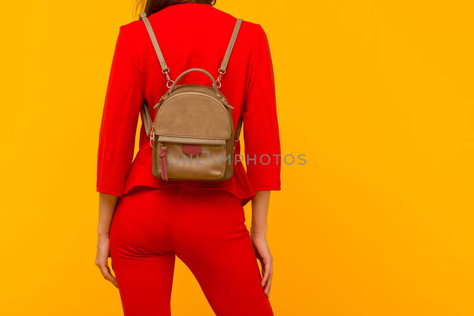 Young girl in a red suit with a small backpack on a yellow background - image