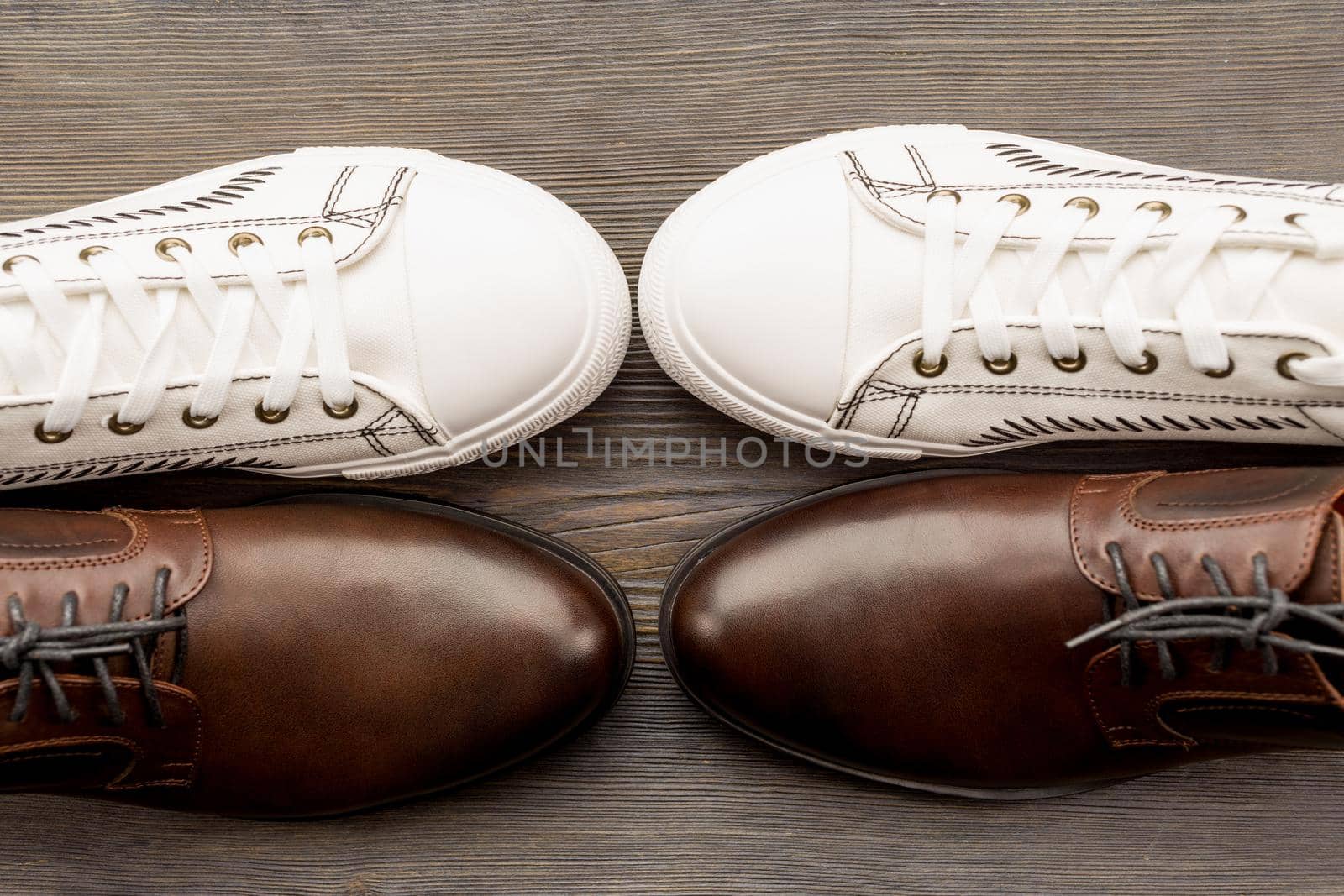 Men's classic brown shoes and white sneakers on a wooden background. Top view by zartarn