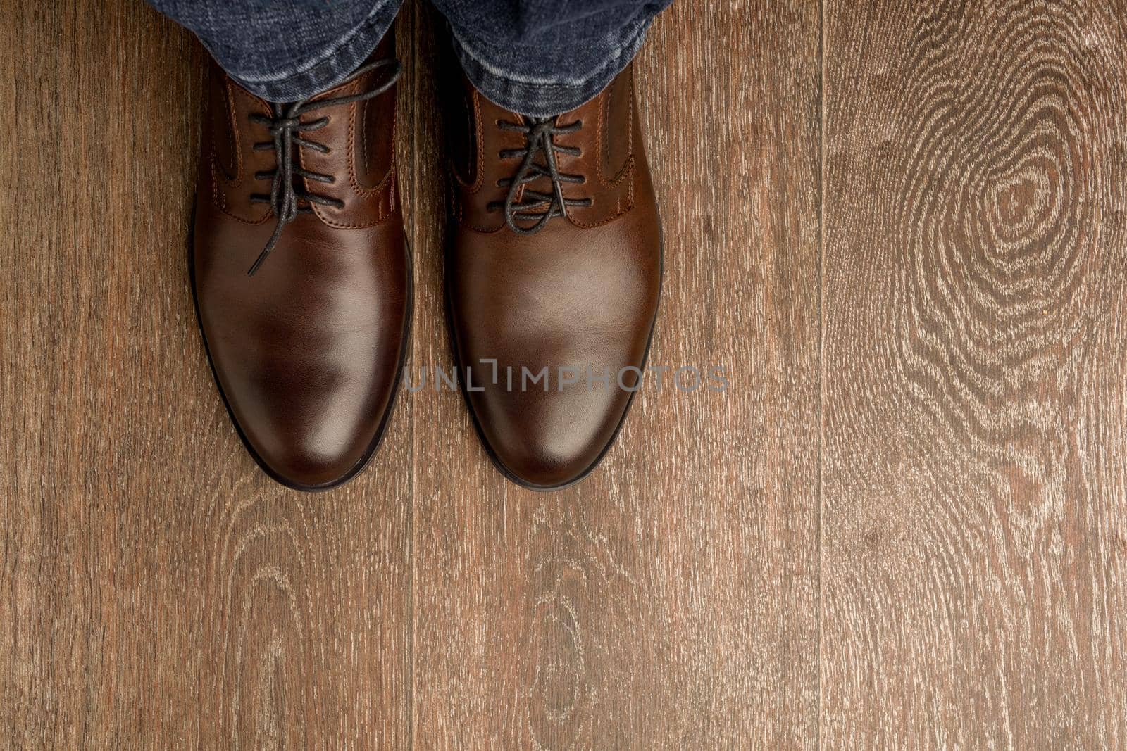 The man wears brown classic shoes on wooden flour. - image