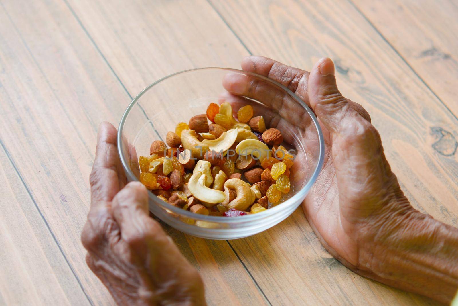 senior women hand hold a bowl of many mixed nuts .