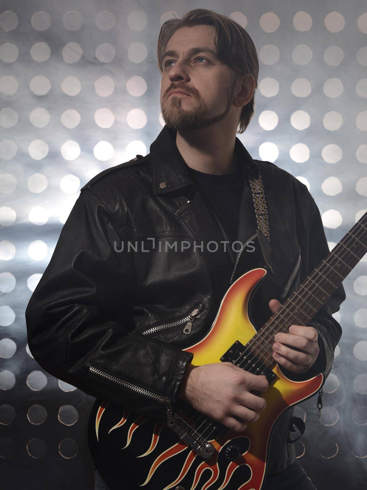 Attractive bearded man with glasses and black leather jackets plays guitar in smoke