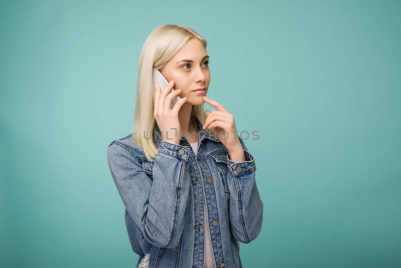 Pensive blonde girl speaks on smartphone isolated on blue background by zartarn