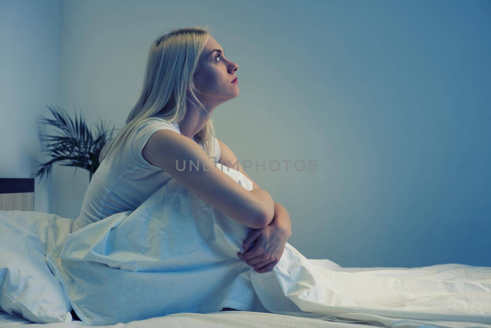 Sad depressed woman sitting in her bed late at night, she is pensive and suffering from insomnia by zartarn