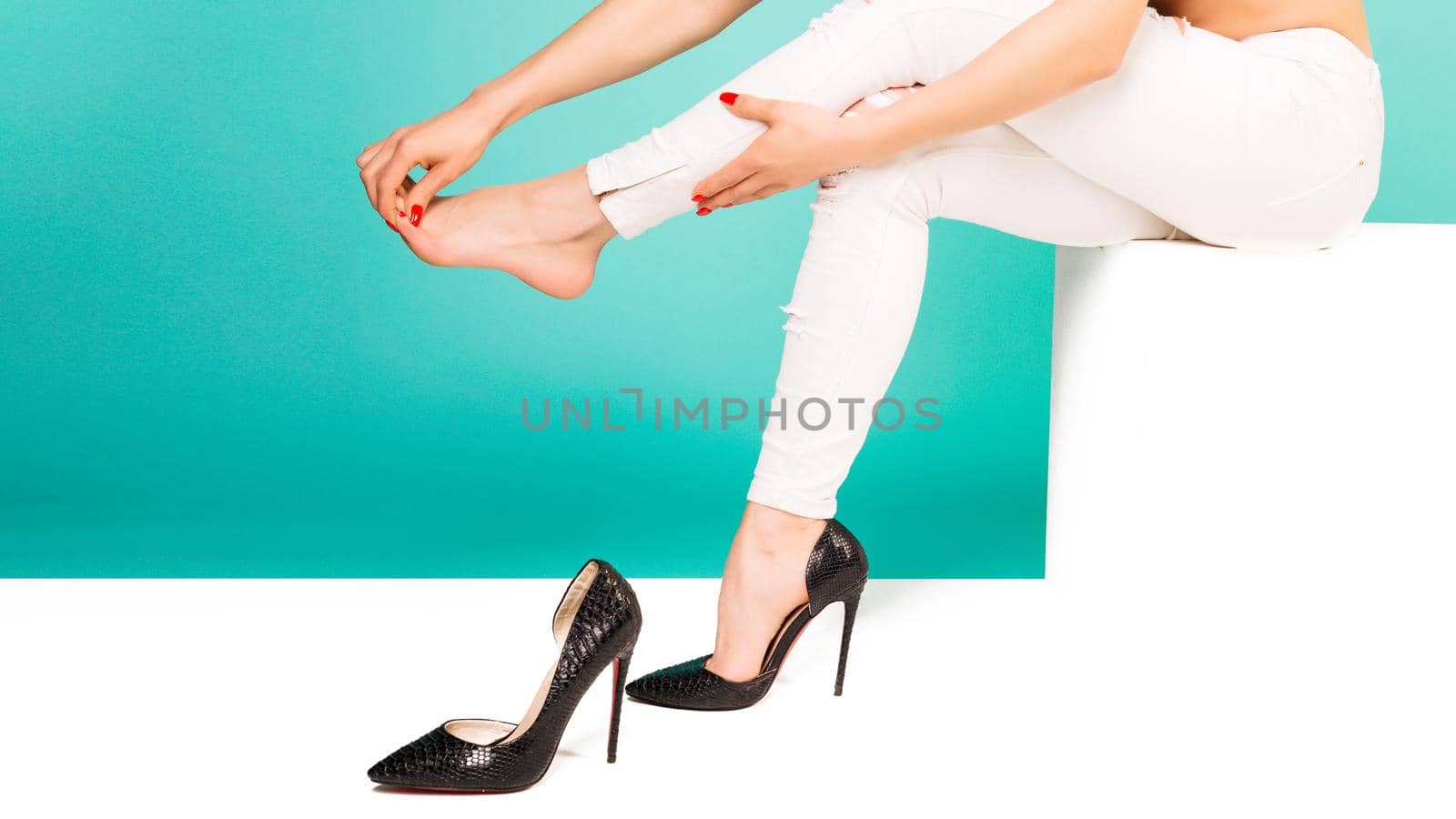 Young woman with slim legs feeling ache because of wearing high heels. Closeup young woman massaging toes on blue background. Healthcare and medical concept.