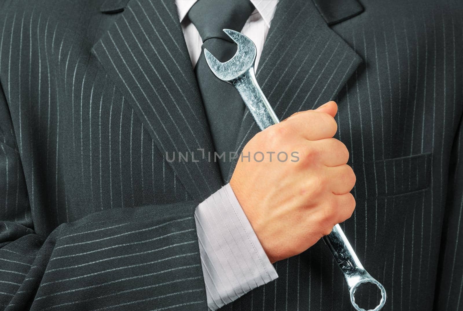 Businessman in a suit holds metal wrench, concept of business creation