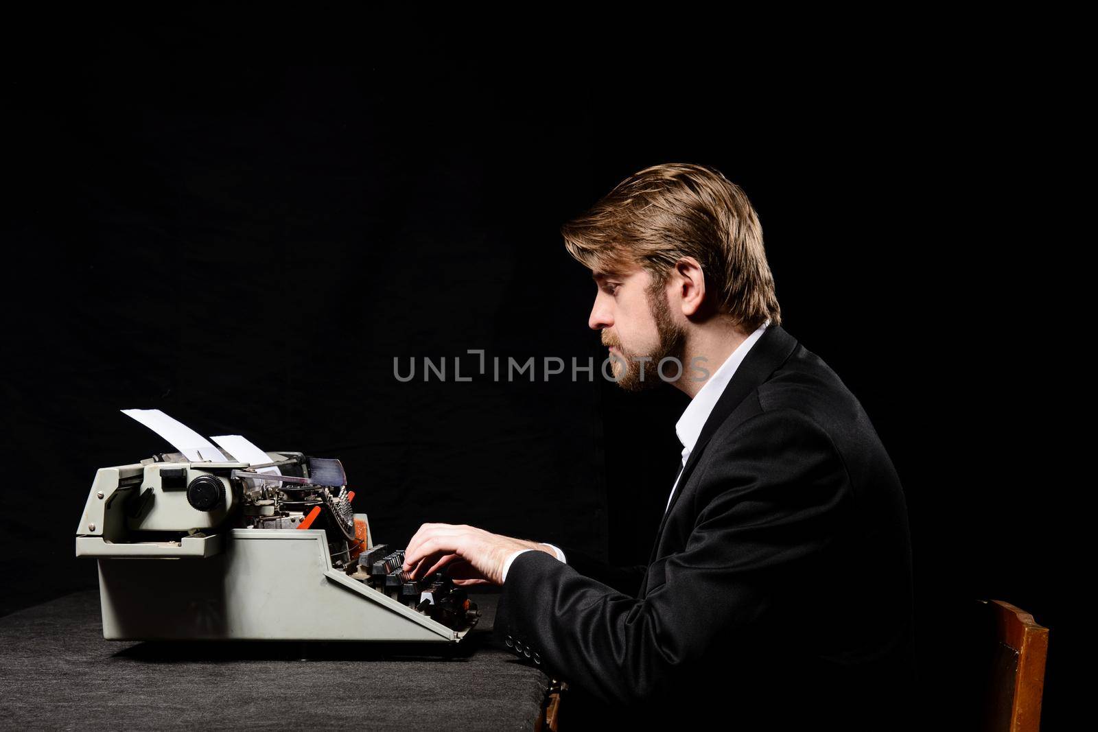 writer, a man in a black jacket typing on typewriter on a black background