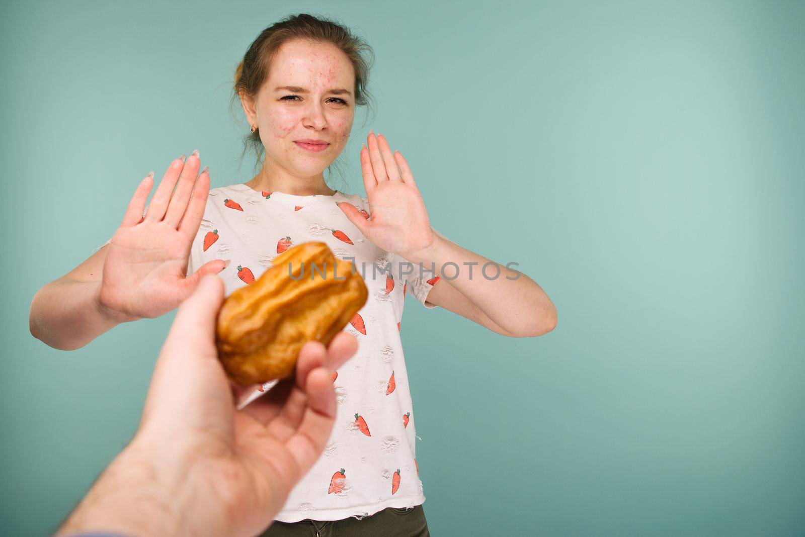 Portrait of pimply teen girl hows hands stop on a delicious cake on blue background