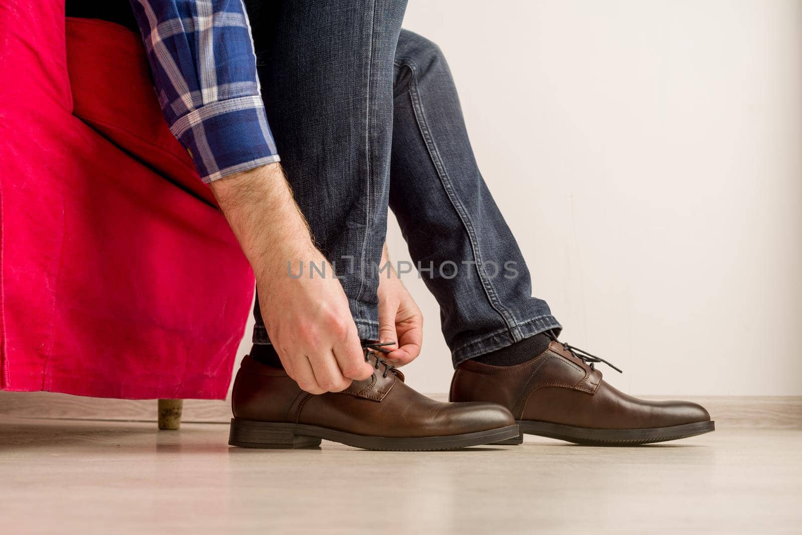 A man in a stylish brown shoes, tying laces is sitting on a red chair - image