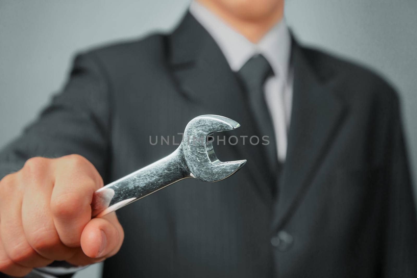 Businessman in a suit holds wrench, focus on wrench, concept of business creation