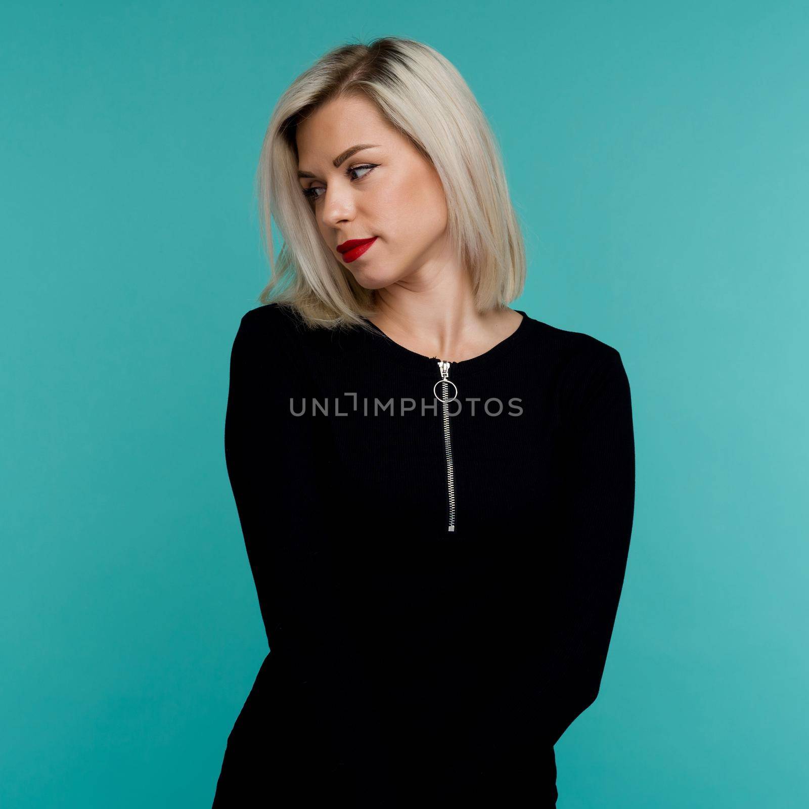 Portrait of an attractive blonde woman in a black dress. Lovely girl posing on a blue background.