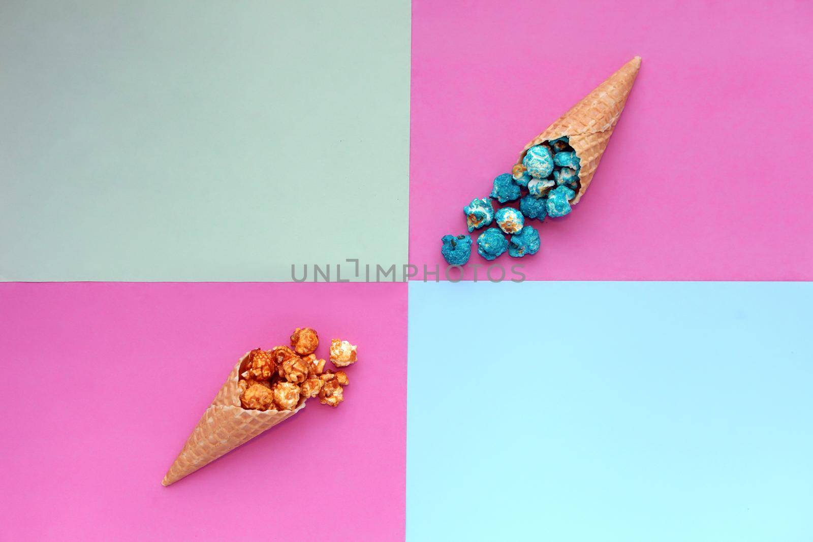 Popcorn spill out from waffle ice cream cone on pastel colorful background. Blue and caramel Popcorn on a cone cornucopia Top view bright hipster background. Fast food. by julija