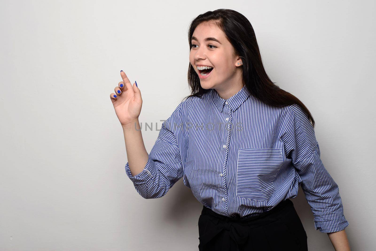 Excited young woman pointing her finger towards blank space standing at white wall