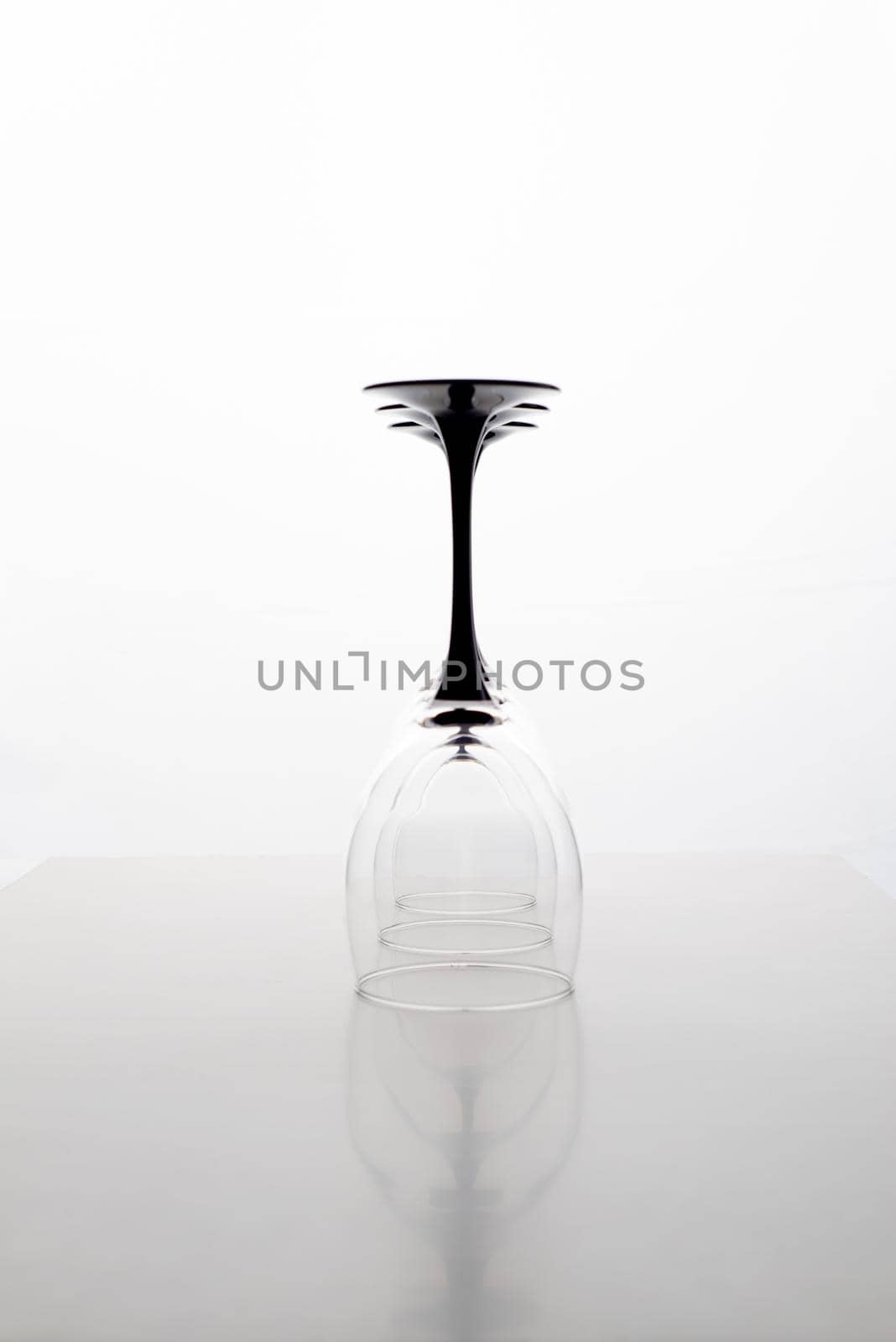 Closeup of three transparent clear crystal empty three inverted wine glasses grey background, vertical picture