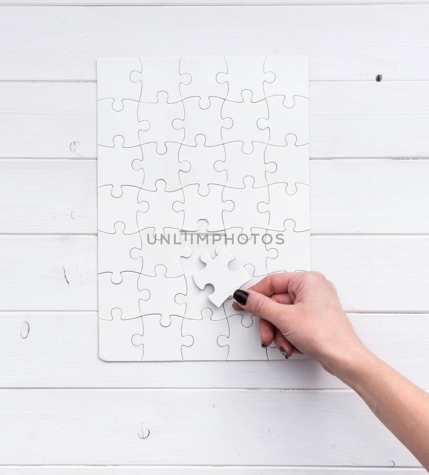 hand holding a piece of white uncompleted puzzle on white wooden background
