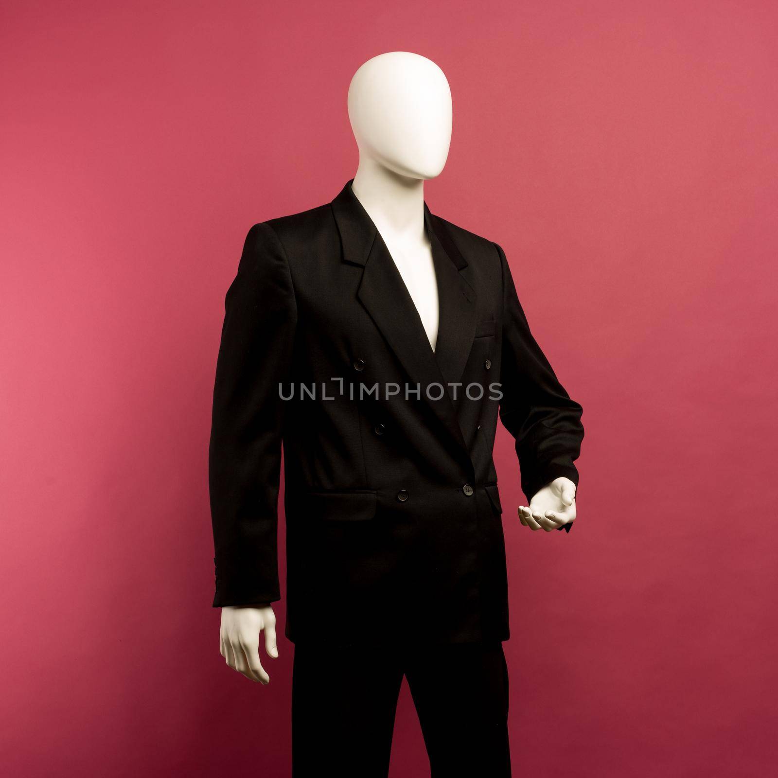 White male mannequin in a black business suit on a ruby background - image