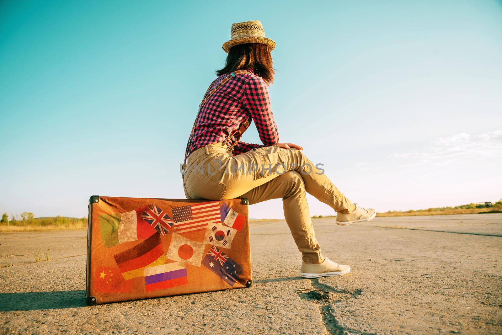 Traveler sits on suitcase with stamps flags by alexAleksei