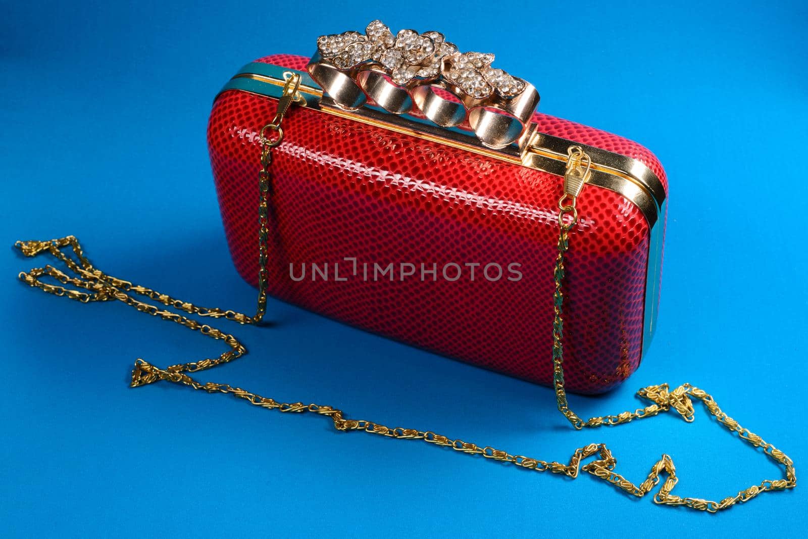 Red handbag clutch with chain on blue background.