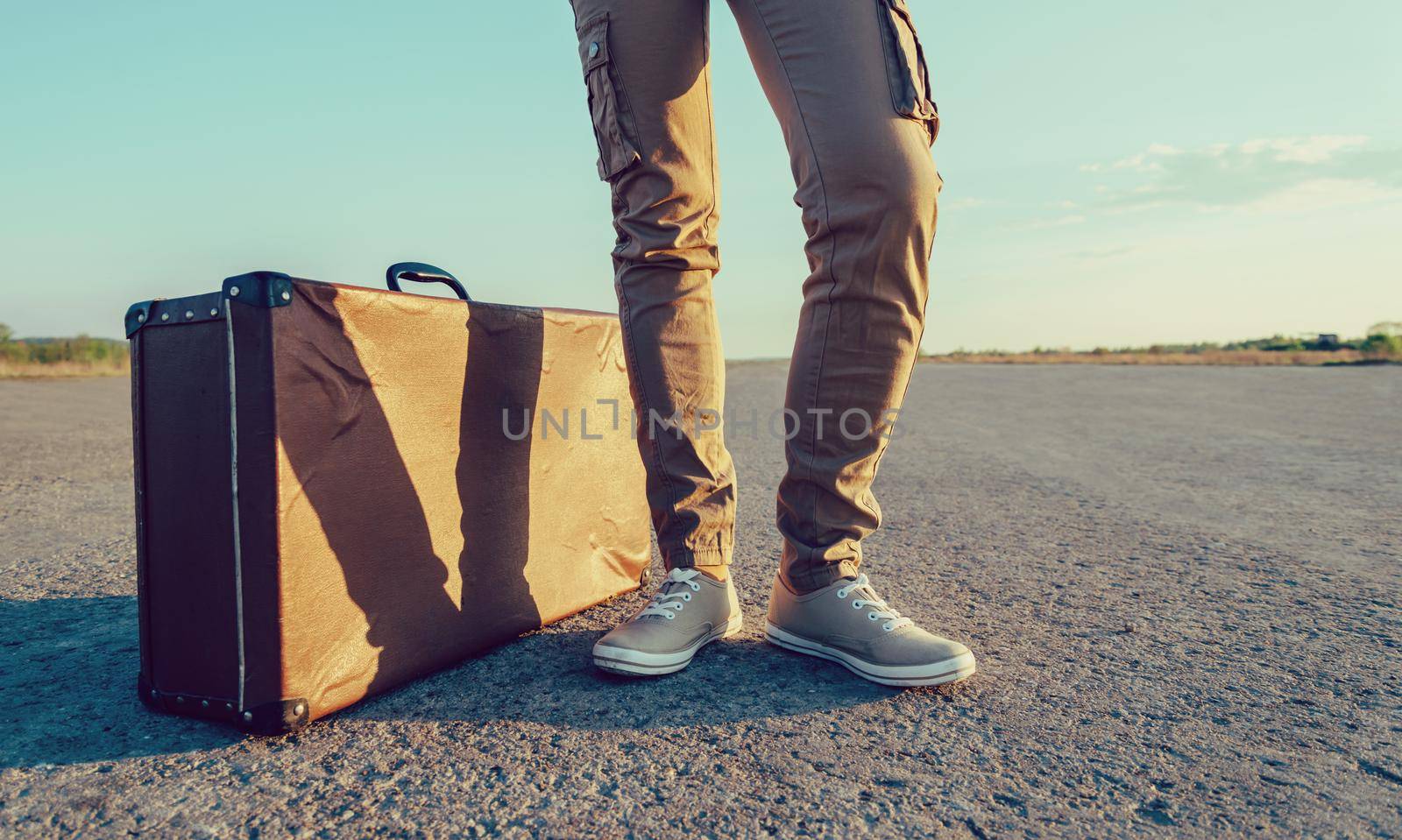 Traveler stands near the vintage suitcase on road, face is not visible. With vintage filter